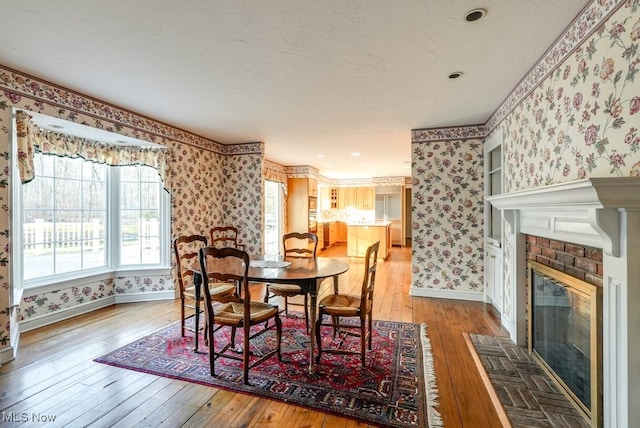 dining space featuring a fireplace, wallpapered walls, baseboards, and wood-type flooring