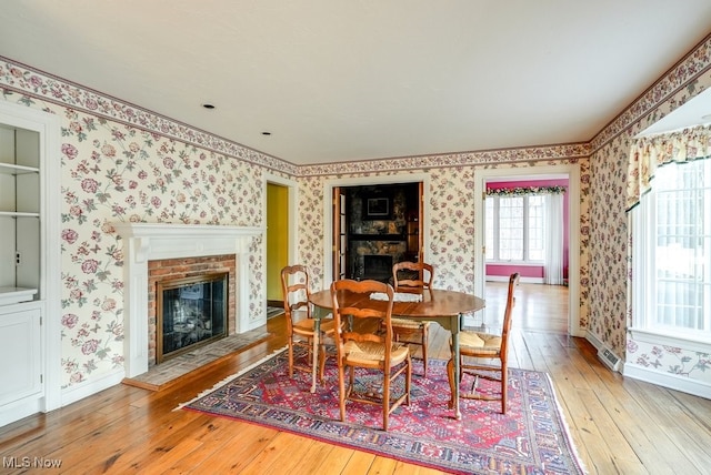 dining space featuring baseboards, hardwood / wood-style floors, a fireplace, and wallpapered walls