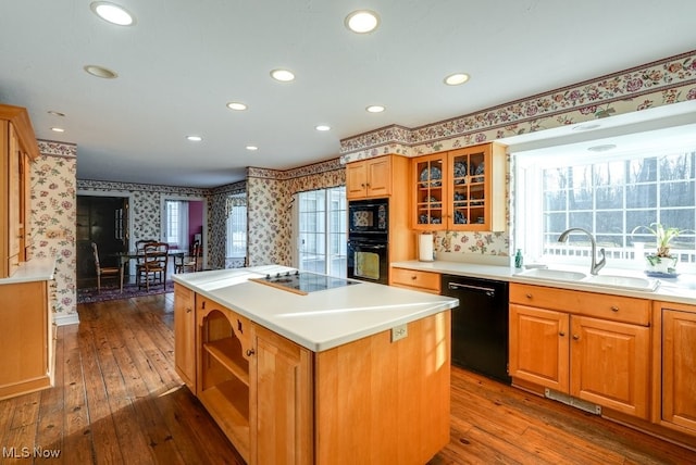 kitchen featuring black appliances, a sink, a kitchen island, wallpapered walls, and dark wood-style flooring