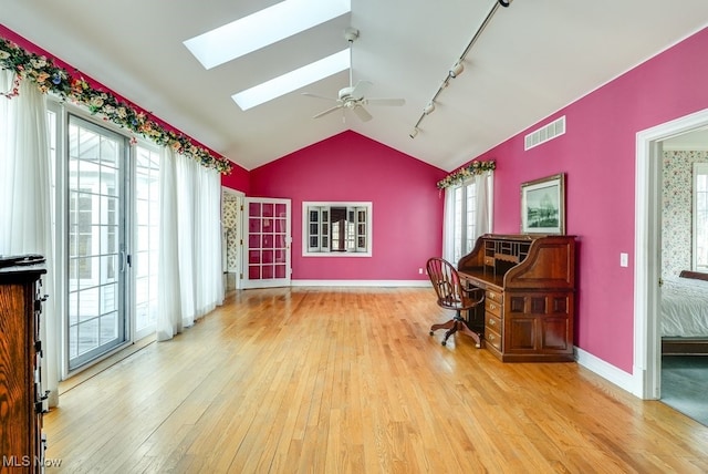 home office with visible vents, hardwood / wood-style flooring, vaulted ceiling with skylight, baseboards, and ceiling fan