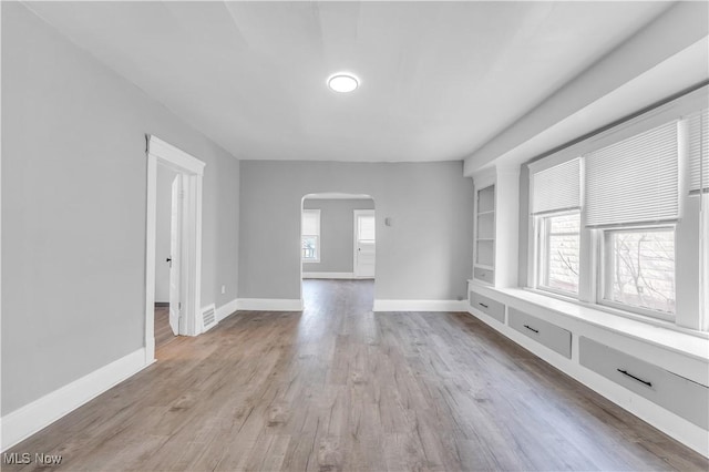 unfurnished room featuring visible vents, wood finished floors, arched walkways, and baseboards