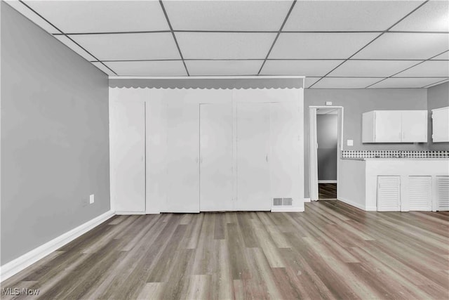 unfurnished living room featuring baseboards, a paneled ceiling, visible vents, and wood finished floors