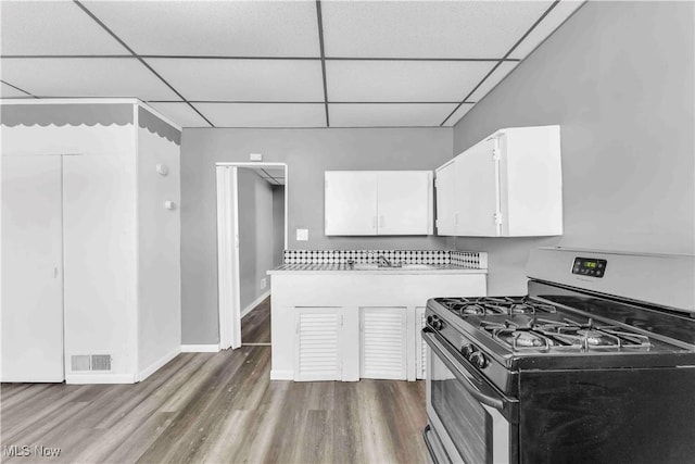 kitchen featuring wood finished floors, gas stove, light countertops, white cabinets, and a paneled ceiling