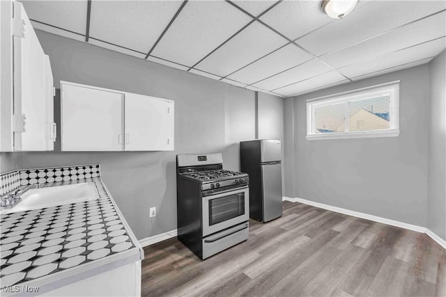 kitchen with wood finished floors, a drop ceiling, a sink, white cabinets, and appliances with stainless steel finishes