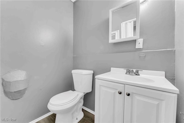 half bath with toilet, vanity, baseboards, and wood finished floors