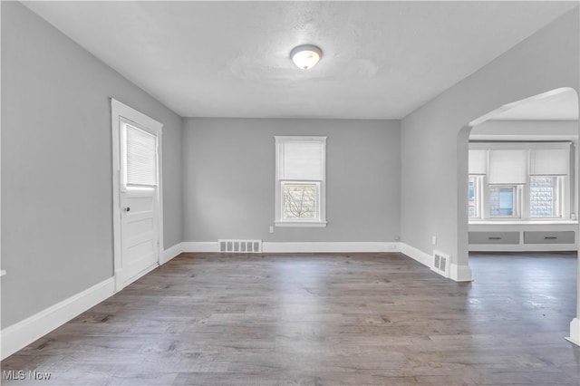 unfurnished room with arched walkways, visible vents, baseboards, and wood finished floors