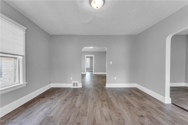 spare room featuring arched walkways, visible vents, and wood finished floors