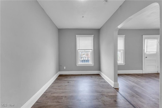 spare room with arched walkways, baseboards, and wood finished floors