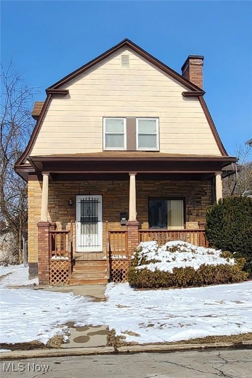 view of front of house featuring stone siding, covered porch, a chimney, and a gambrel roof