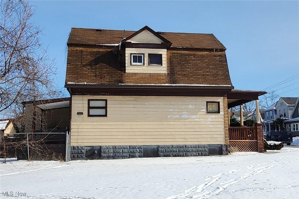 view of snow covered exterior featuring roof with shingles and fence