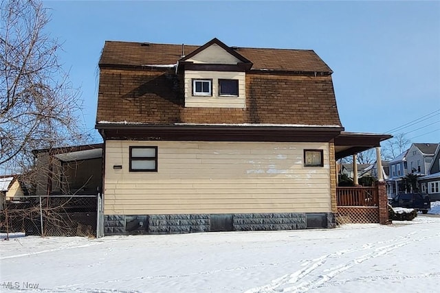 view of snow covered exterior featuring roof with shingles and fence