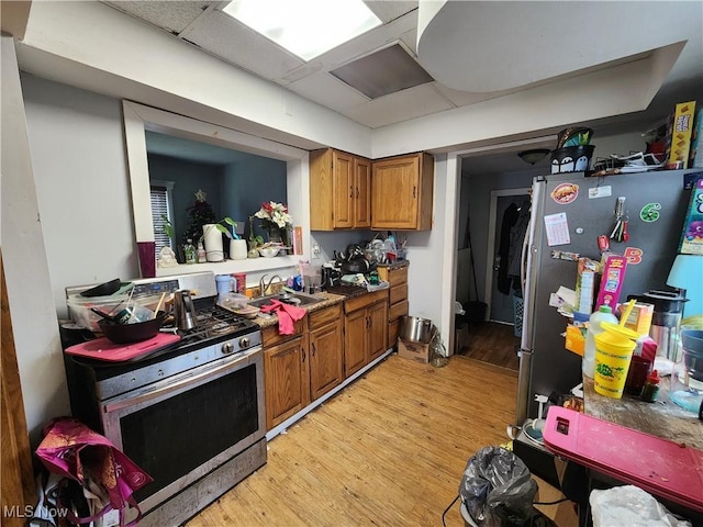 kitchen featuring brown cabinets, a sink, a drop ceiling, stainless steel appliances, and light wood finished floors