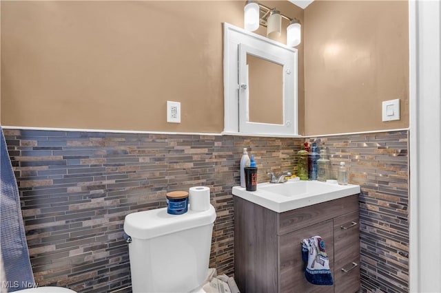 half bath with vanity, tile walls, toilet, and a wainscoted wall