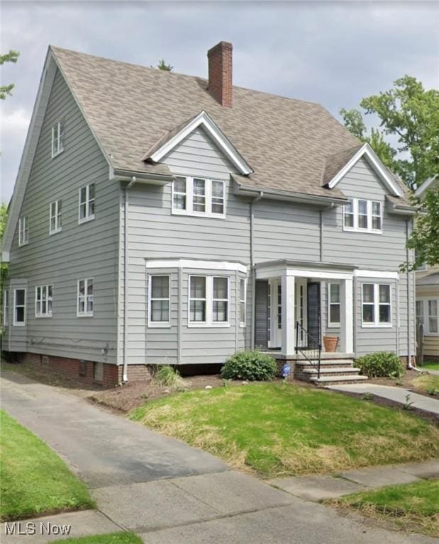 view of front of property featuring a shingled roof, a front lawn, and a chimney