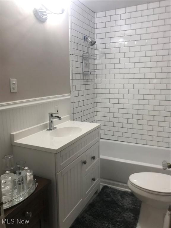 bathroom featuring washtub / shower combination, vanity, toilet, and wainscoting