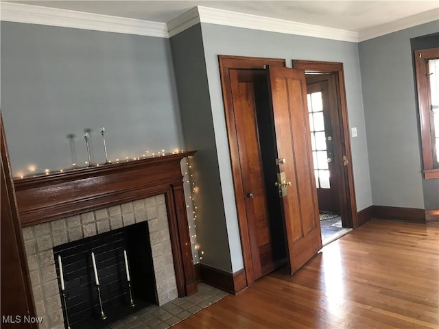 entryway with baseboards, wood finished floors, a fireplace with flush hearth, and ornamental molding