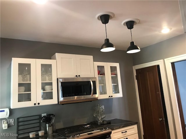 kitchen featuring dark countertops, stainless steel microwave, white cabinets, and glass insert cabinets