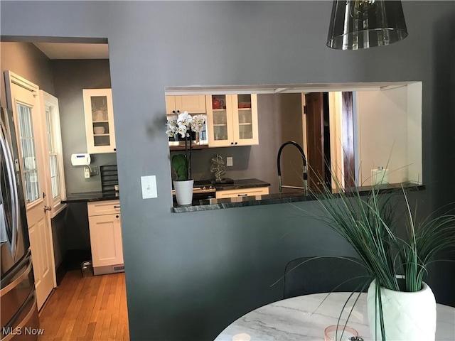 kitchen featuring light wood-type flooring, stainless steel microwave, dark countertops, white cabinetry, and glass insert cabinets