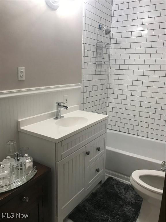 bathroom with a wainscoted wall, shower / bathtub combination, toilet, and vanity