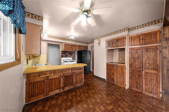 kitchen with a sink, freestanding refrigerator, a peninsula, white range with gas stovetop, and ceiling fan