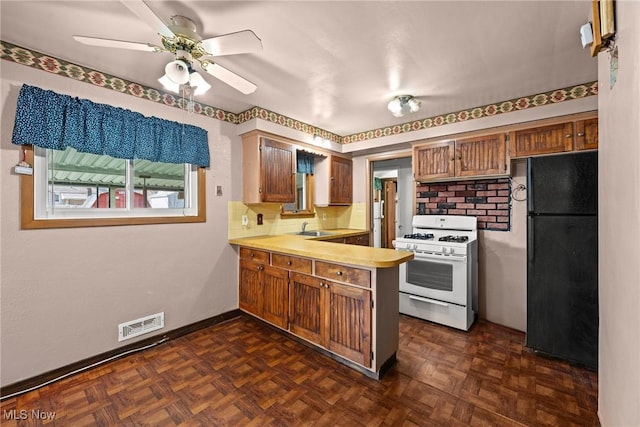 kitchen with visible vents, white gas range, a peninsula, freestanding refrigerator, and a sink