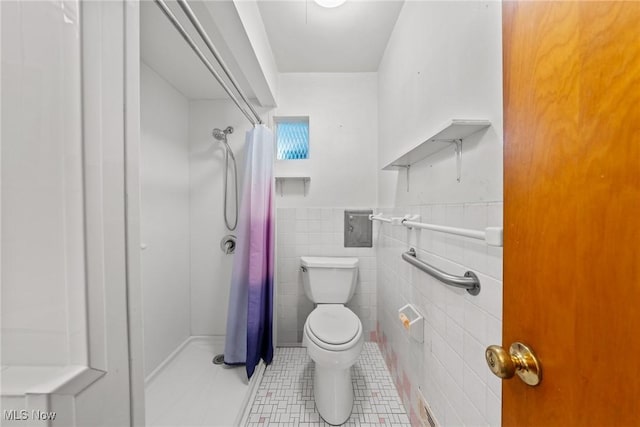 bathroom featuring toilet, curtained shower, tile walls, wainscoting, and tile patterned flooring