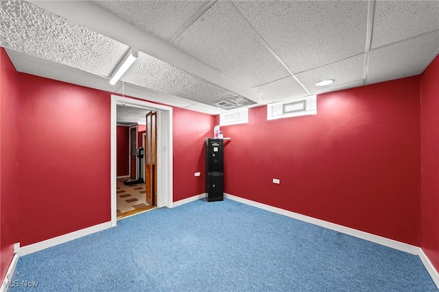 basement with carpet flooring, a paneled ceiling, and baseboards