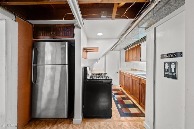 kitchen with range with gas cooktop, light floors, light countertops, brown cabinets, and freestanding refrigerator