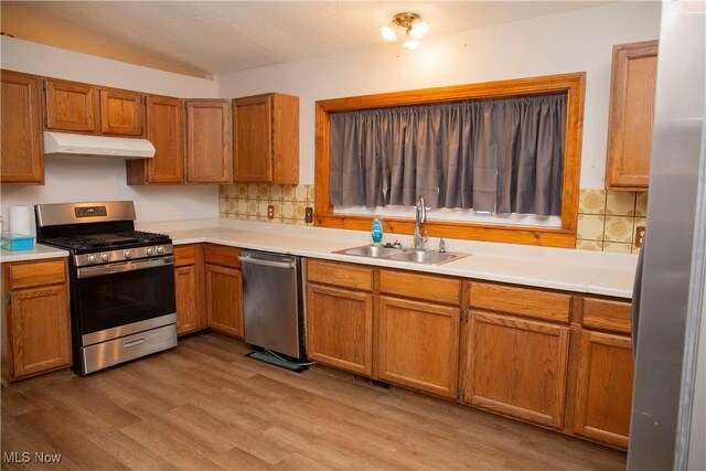 kitchen with tasteful backsplash, appliances with stainless steel finishes, under cabinet range hood, and a sink