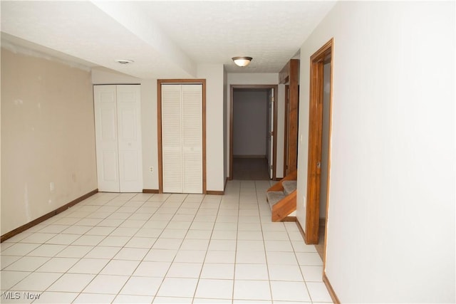corridor featuring light tile patterned floors, baseboards, a textured ceiling, and stairway