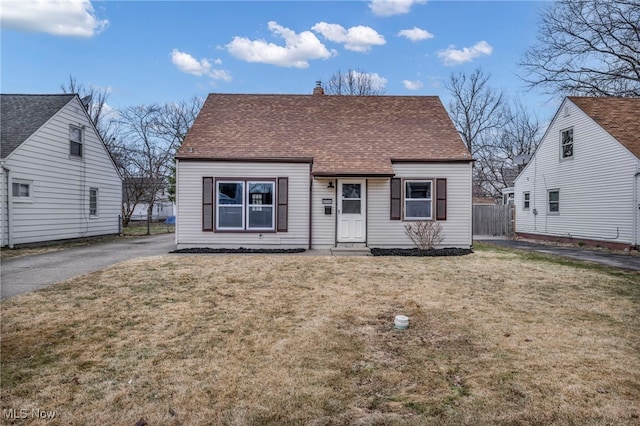 view of front of house with a chimney, a shingled roof, a front lawn, and fence