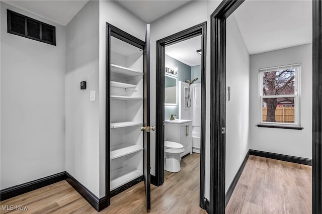 hallway featuring visible vents, light wood-type flooring, and baseboards