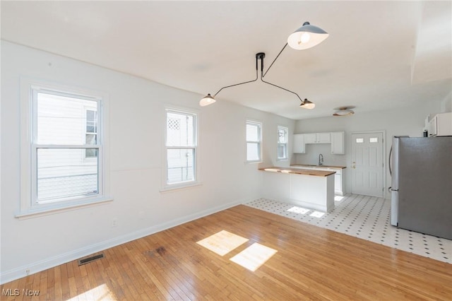kitchen with visible vents, baseboards, a peninsula, freestanding refrigerator, and white cabinetry