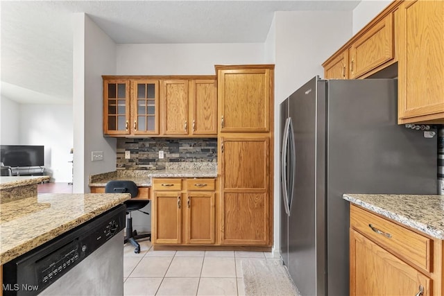 kitchen featuring light stone counters, light tile patterned flooring, glass insert cabinets, appliances with stainless steel finishes, and backsplash