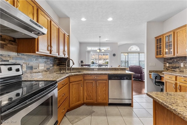 kitchen featuring light tile patterned floors, a peninsula, a sink, stainless steel appliances, and under cabinet range hood