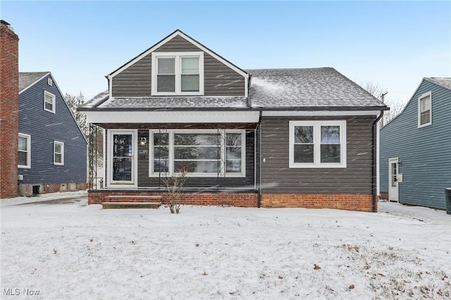 snow covered back of property featuring central air condition unit, a porch, and a shingled roof