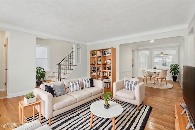 living area with stairs, light wood-style floors, and baseboards