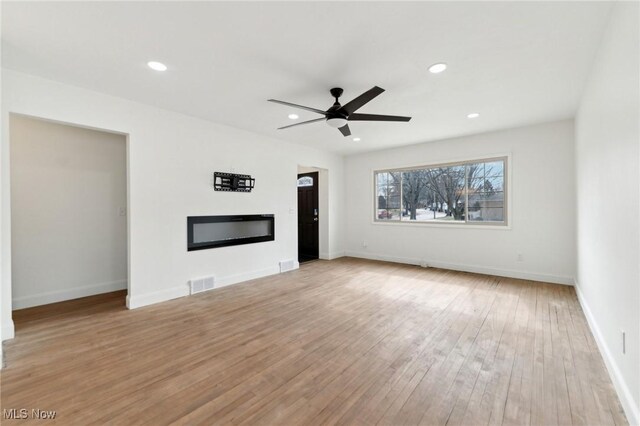 unfurnished living room with recessed lighting, a glass covered fireplace, light wood-style flooring, and baseboards