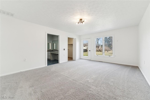 unfurnished bedroom with a walk in closet, visible vents, a textured ceiling, carpet floors, and baseboards