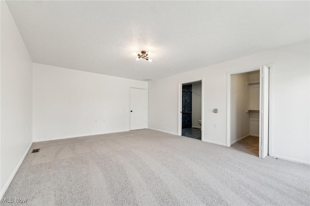 unfurnished bedroom with carpet flooring, baseboards, a walk in closet, and visible vents