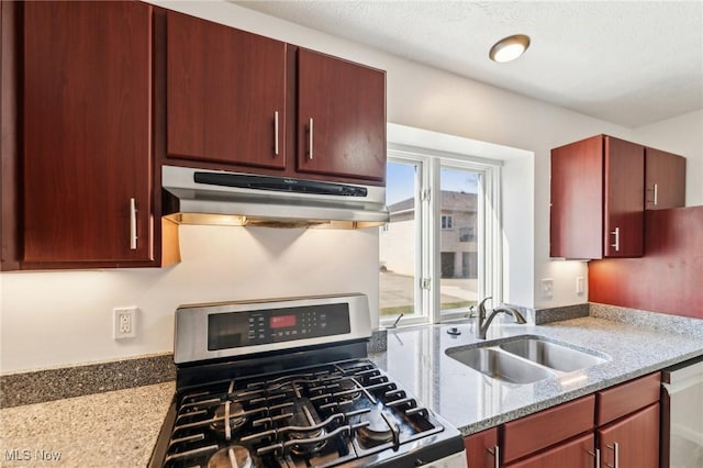 kitchen with gas range, light stone countertops, under cabinet range hood, and a sink