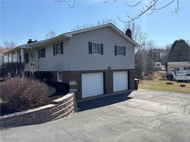 view of side of home with a garage, driveway, brick siding, and a chimney