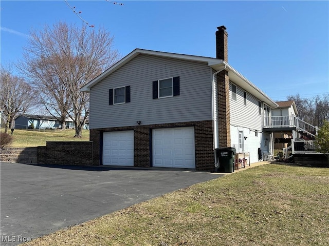 view of property exterior with driveway, a yard, an attached garage, brick siding, and a chimney