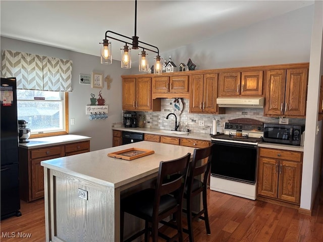 kitchen featuring a sink, black appliances, light countertops, under cabinet range hood, and brown cabinets