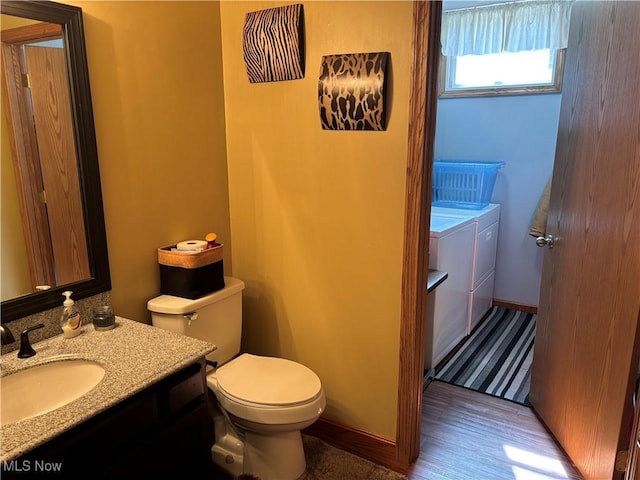half bath with vanity, wood finished floors, baseboards, toilet, and independent washer and dryer