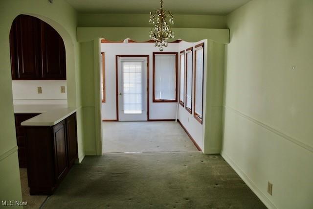 interior space featuring light carpet, baseboards, and a chandelier