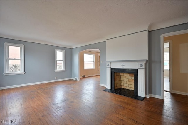 unfurnished living room featuring baseboards, arched walkways, wood-type flooring, and a fireplace with raised hearth