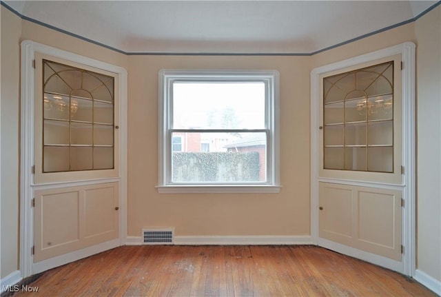 spare room with wood finished floors, visible vents, and baseboards