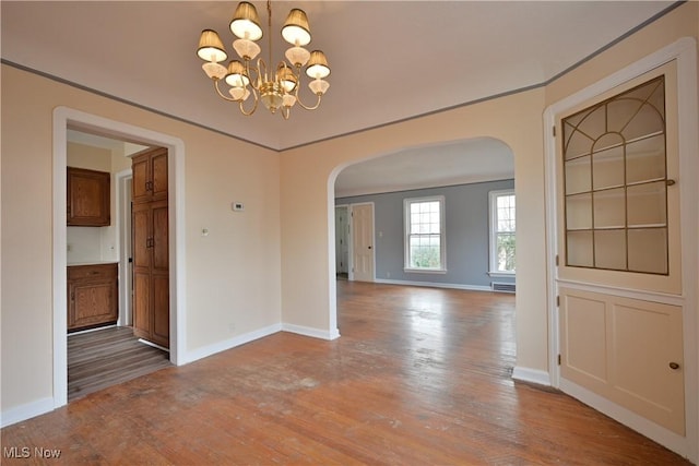 unfurnished dining area with baseboards, wood finished floors, arched walkways, and a chandelier