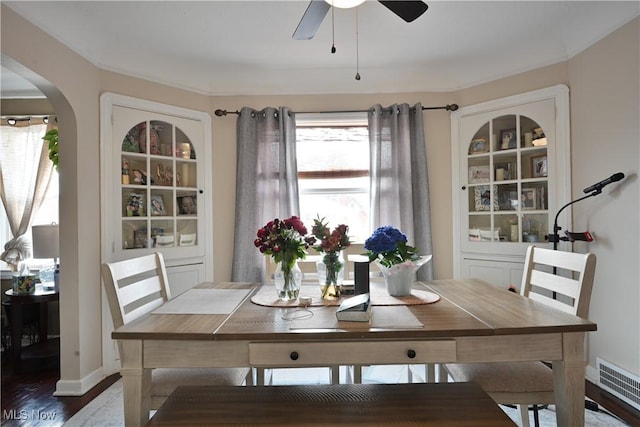 dining space featuring visible vents, built in shelves, dark wood finished floors, arched walkways, and a ceiling fan